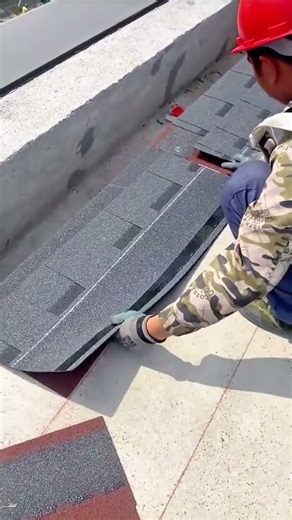 Professional roofing worker hammering asphalt shingles onto a concrete roof surface