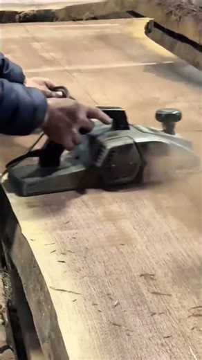 smoothing the surface of a large wooden slab using an electric hand planer in a carpentry workshop