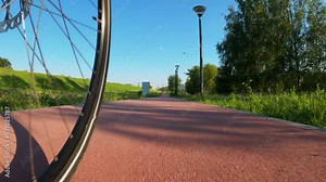 Low angle point of view of a bicycle wheel rolling on a paved bike path thru a park at evening
