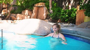 Young happy woman swimming in Japanese spa stone pool with colorful blue water in Japan onsen inside beauty health