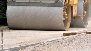 Footage of a road roller leveling a soil substructure for a new walkway in an urban settlement