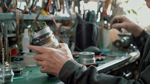 Hands with screwdriver repair photo camera lens on a table with many spare parts and tools. Old film workshop Professional technician with tool carefully remove small screws of lens on workplace