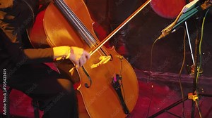 A close-up of rapid cello playing. A bright light show. A woman's hand with a bow quickly drives on the strings of the cello. Symphonic concert of classical music