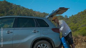 Man with clothes close the car trunk. A man takes the tent by the car trunk in nature during sunny trip.