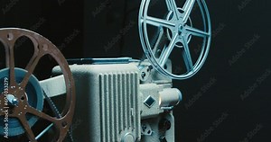 Old Movie Projector in Close up. Antique Movie Projector With 8mm Spinning Film Reels. Spinning Film Roll on a Vintage Film Projector. Light Beams From Film on an Old Projector