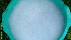Point of view 4k video shot of woman doing washing of clothes outdoor in backyard. Closeup of female hands in pink gloves and green plastic basin with foamy water after adding detergent powder into it