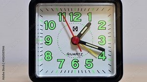 Zoom out time lapse video of a plastic alarm clock on a wooden surface.