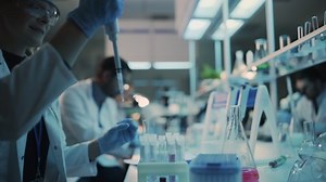 Close Up of a Female Research Scientist Using Micropipette to Mix Liquids in a Test Tube in a Modern Laboratory. Scientists are Conducting Research with the Help of Microscope and Tablet Computer.