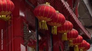 From below of red traditional Chinese lanterns hanging and swaying on roof of building in city during daytime