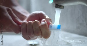 Hands rinsing toothbrush under water. Man washes toothbrush bristles under tap water in bathtub in sink from excess toothpaste. Need to keep toothbrush clean to prevent bacteria from growing concept.
