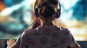 A child or teenager is playing an unrecognizable computer video game on a large blurry screen. Online video game technology and teen gambling addiction to video games