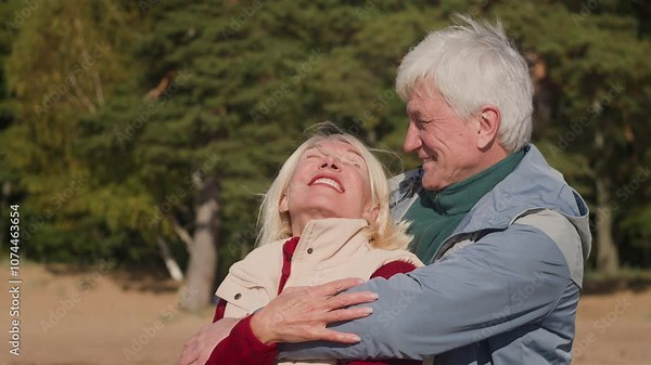 Senior elderly couple stay on beach, hugging and enjoying leisure together. Tender love of old married couple embraces during stroll along seaboard, smiling and admiring nature. Retired marital pair