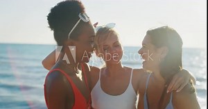 Young multi-ethnic girlfriends in bikinis are having fun to enjoy their summer vacation together on a beach with a sea on a sunset.