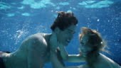 Medium shot of young couple kissing under water in pool. They are...