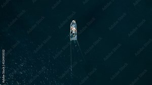 Top view on small trawler boat moving in ocean with deep blue water. Fishermen ready to pull trawl net on board