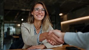 Agreement handshake: A poised professional woman in glasses and blazer seals a deal with a firm handshake, a symbol of trust and collaboration in a modern office environment.