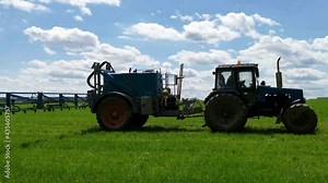 Spraying a green wheat field by tractor. The farming tractor spraying on field with sprayer, herbicides and pesticides. Industrial machine fertilizing a field. Side view.