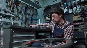 Male bicycle mechanic in repair shop making repair of bike wheel. Replacing rear hub bearings. Reassembly of cycle hub ball bearings and lubricating. Cycle repairman at work. Technician in workshop.