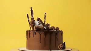 KYIV, UKRAINE - January 15: Birthday cake with brown cream cheese frosting, chocolate drips decorated with Kinder egg, Milka and KitKat, Oreo cookies and candies. Cake rotating on yellow background
