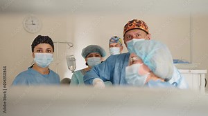 Team of surgeons performing operation in hospital. Surgeon male healthcare professional in a hospital operating theatre wearing a surgical cap and mask. Female doctor in medical uniform putting