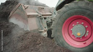 Close up of a wheel loader driving towards a compost heap loading his shovel.