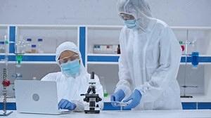 African american scientist using laptop colleague with samples in laboratory