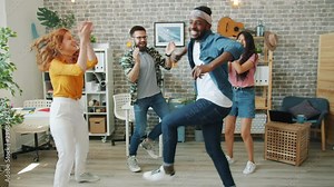 Excited young people girls and guys are dancing at corporate party clapping hands chilling in modern office. Happiness, work and entertainment concept.