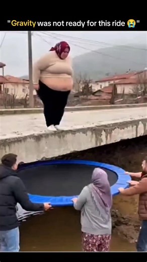 Knowledge Matrix on Instagram: "The post features a short clip showing a woman wearing a headscarf standing on a concrete ledge above a muddy stream while two men and another woman below hold a large, round portable trampoline. She prepares to jump with her arms spread, then leaps toward the trampoline, but upon landing the trampoline folds and collapses instead of bouncing. The woman falls straight into the muddy water below, creating a large splash that covers everyone nearby as the holders lo