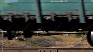 Side view of a freight train moving on rails with beautiful natural landscape on the background. Stock footage. Close up for moving cargo train in front of green trees and mountains.