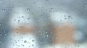 Rain drops pouring down on window glass with urban city skyline view on a rainy weather day