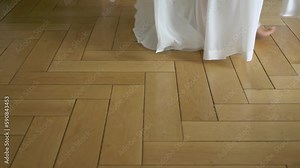 A bride in a long white wedding dress walks barefoot on wooden floor. Woman in gown at vacation or at home. Wedding ceremony, reception.