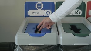 Throwing a piece of paper in a special bin for waste recycling, concept of ecology. HDR. Close up of male hand putting a small sheet of paper in a recycling bin.