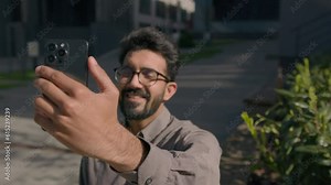 Arabian businessman smile talk video call use mobile phone technology business communication outdoors in sunny city happy guy Indian man employer leader entrepreneur talking distant happy greet online