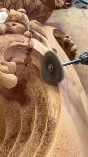 An artisan uses a rotary tool to carve intricate details into a large wooden piece