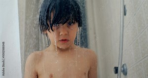 Child stands in the shower with water cascading down, captured in ultra slow-motion at 800 fps. child gazes with a thoughtful expression, creating a serene and calming moment under the shower