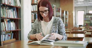 Attractive young woman is reading a book in the reading room of the library.