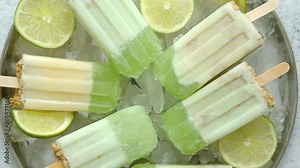 Summer refreshing homemade lime popsicles with chipped ice over stone background