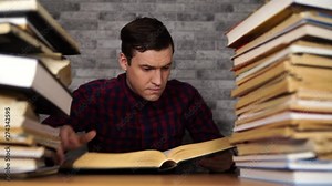 Man student boring reading book at library with a lot of books in university. Student disheartened reading book for examination.