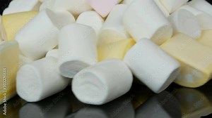 Multicolored mini marshmallow candies rotation slowly on a mirror surface and a black background. The problem of diabetes and overeating sweet.
