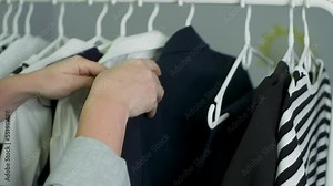 Woman is choosing her outfit for office job moving hangers with clothes, hands close-up. She thinks what to wear. Clothing wardrobe fashion trend concept. Everyday office style apparel for work. Stock Video