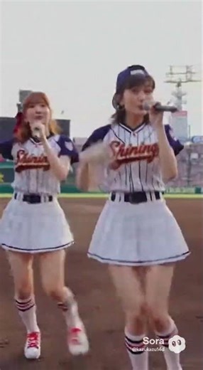 A Japanese two-member female idol duo performing a song at a baseball stadium.