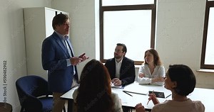 Middle aged team leader speaking to group, presenting new strategy, plan of project, telling idea to listening employees at table. Mentor, coach giving corporate training