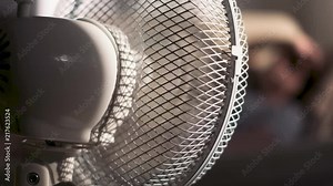 Heat concept, blowing cooling fan close up, girl severing from high temperature in the background, 4K UHD