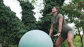 A pregnant woman exercises outdoors, balancing on a stability ball...