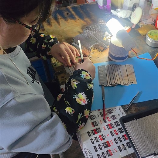 Do you think most harmonica players know how much work goes into making and tuning their beloved instruments? Here she's making sure the reeds are centered in the slot. And even though she's enjoying some jams, it's still hard work! | Bushman Harmonicas