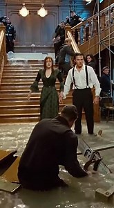 This behind-the-scenes moment captures the staggering intensity of the flooded grand staircase collapse rehearsal inside the Titanic set, where elegance and destruction collide in one breathtaking test run. The iconic staircase—rebuilt full-scale with polished railings, chandeliers, and ornate paneling—stands quietly under studio lights until the water rigs ignite. In seconds, a massive surge bursts through the upper doors, thundering down the steps as furniture, props, and decorative pieces are
