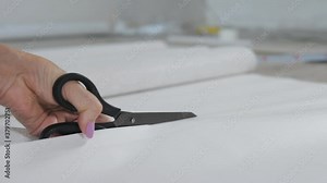 Close-up of a woman's hand cutting a sheet of Wallpaper with scissors for later pasting it on the wall.