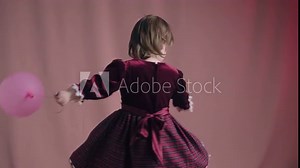 Cute little girl in an vintage burgundy dress is playing with a pink inflatable balloon. The concept of children theater productions and developing acting circles. Fuchsia color background