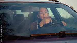 Woman expresses variety of emotions while driving, showing feelings of happiness, sadness, anger, and frustration while riding in car. Swears and shouts at other drivers and people.