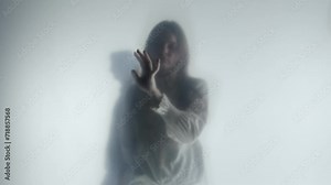 Melancholic female silhouette behind a transparent frosted curtain or glass close up. A woman guides her hand on the surface of the curtain, while a male silhouette passes behind her back.